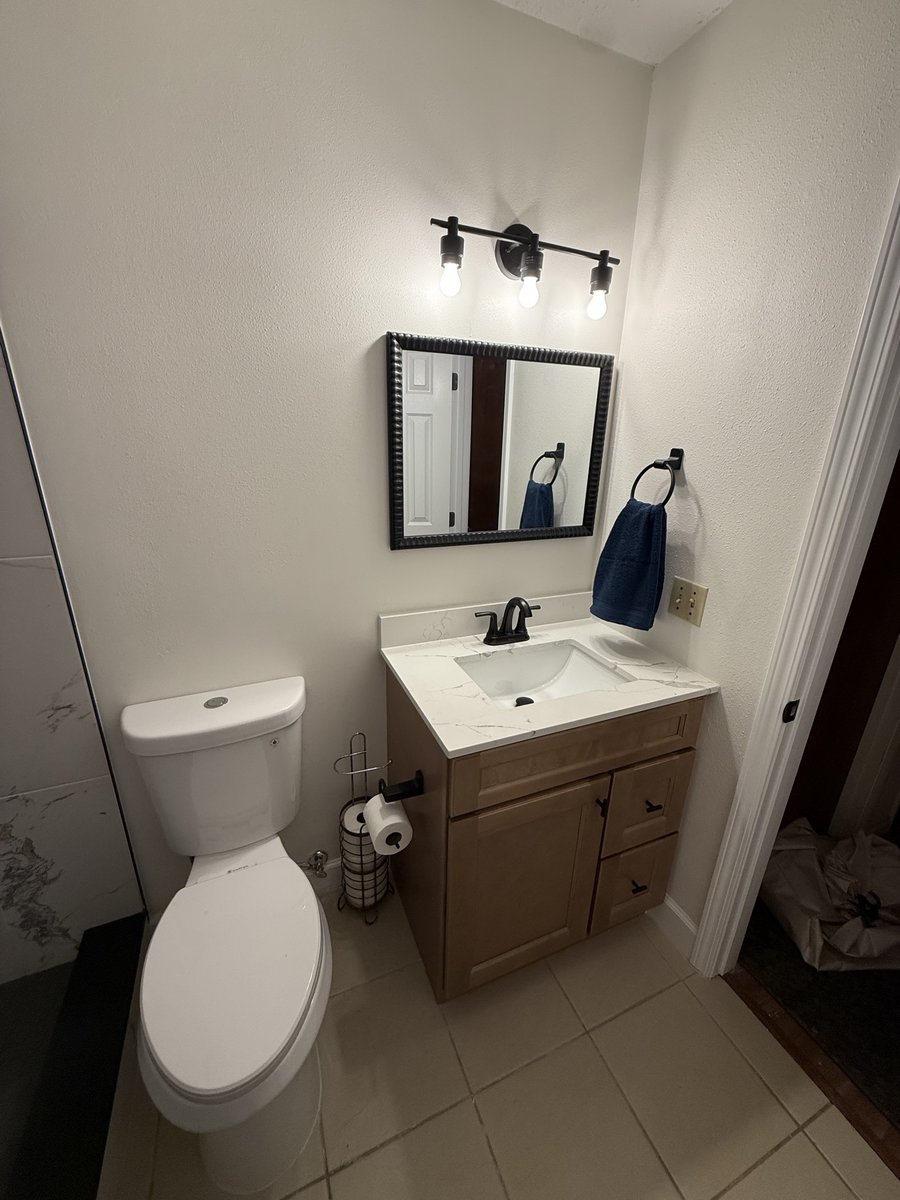 Bathroom vanity installed by KM — light wood cabinet, marble-look countertop, mirror, and black fixtures